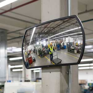 Industrial convex safety mirror mounted on a warehouse wall overlooking a busy forklift aisle.